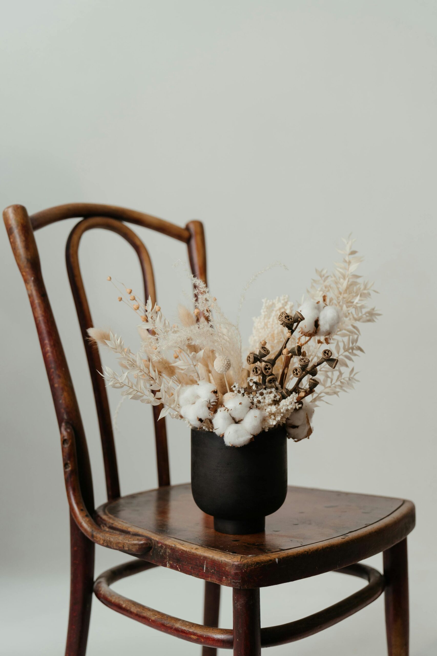 Vase mit Trockenblumem steht auf Holzstuhl